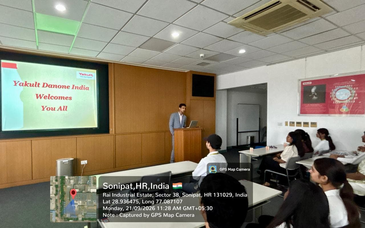 Yakult Danone India presenter at a podium beside a 'Welcomes You All' slide